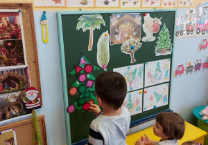 Dzieci przy tablicy ozdabiają choinkę klasyfikując bombki wg kształtu i koloru.